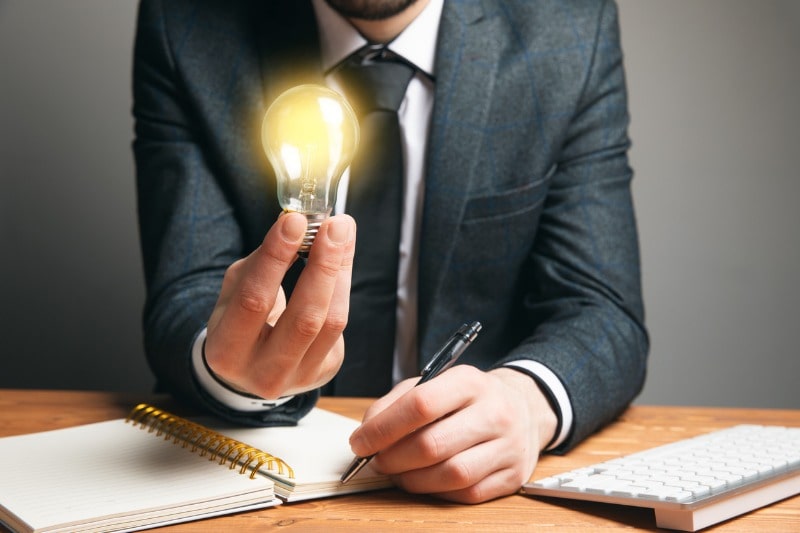 Employer holding a lighted lightbulb in his right hand to light his path to find the best rpo companies.